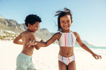 Zwei fröhliche kleine Kinder, die Spaß haben und sich am Strand vergnügen. Zwei bezaubernde ethnische Kinder, die fröhlich lächeln, während sie in Badekleidung herumspielen. - JLPSF09448