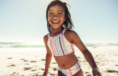 Adorable little girl smiling happily while playing on beach sand. Active little girl having fun and enjoying herself during summer vacation. - JLPSF09450