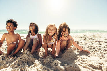 Happy young children smiling cheerfully while playing with sea sand at the beach. Group of adorable little kids having a good time together during summer vacation. - JLPSF09452