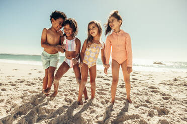 Fröhliche kleine Kinder lachen, während sie zusammen am Strand spielen. Gruppe von entzückenden jungen Freunden, die während der Sommerferien zusammen Spaß haben. - JLPSF09455