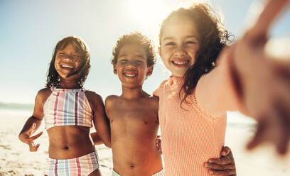 Glückliche kleine Kinder, die fröhlich lächelnd ein gemeinsames Selfie am Meer machen. Liebenswerte kleine Kinder, die ihren Sommerurlaub an einem sonnigen Strand genießen. - JLPSF09464