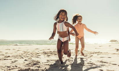 Excited kids laughing happily while running around at the beach. Group of happy kids having fun while playing on beach sand. Adorable little kids enjoying their summer vacation. - JLPSF09465