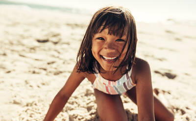 Glückliches junges Mädchen, das in die Kamera lächelt, während es am Strand spielt. Liebenswertes kleines Mädchen, das Spaß hat und sich in den Sommerferien amüsiert. - JLPSF09466