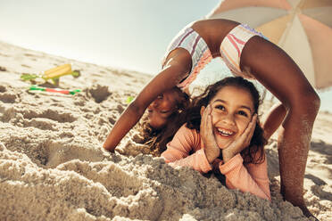 Kreative kleine Mädchen, die sich gemeinsam am Strand vergnügen. Zwei entzückende junge Freundinnen, die fröhlich lächelnd miteinander am Strand spielen. Fröhliche Kinder, die ihren Sommerurlaub genießen. - JLPSF09470