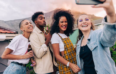 Freunde der Generation Z machen ein Selfie während einer Party auf dem Dach. Eine Gruppe glücklicher Freunde posiert für ein Gruppen-Selfie, während sie Bierflaschen in der Hand halten. Multikulturelle Freunde, die am Wochenende zusammen Spaß haben. - JLPSF09495