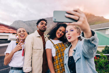Gruppen-Selfie auf dem Dach. Vier glückliche Freunde posieren für ein Selfie beim gemeinsamen Feiern im Freien. Gruppe multikultureller Freunde, die am Wochenende eine gute Zeit miteinander verbringen. - JLPSF09496