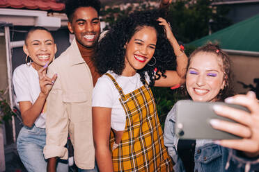 Selfie-Zeit auf dem Dach. Vier glückliche Freunde der Generation Z, die ein Gruppenfoto mit einem Fotohandy machen. Eine Gruppe multikultureller Freunde, die am Wochenende viel Spaß miteinander haben. - JLPSF09501