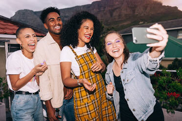 Capturing happy smiles. Four happy generation z friends taking a group selfie on a camera phone. Group of multicultural friends having a good time together on the weekend. - JLPSF09502