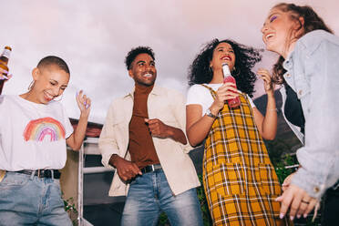 Freunde tanzen auf einer Dachterrassenparty. Eine Gruppe glücklicher Freunde der Generation Z feiert mit einem Bier auf einer Dachterrasse. Vier multikulturelle junge Leute, die am Wochenende zusammen Spaß haben. - JLPSF09504