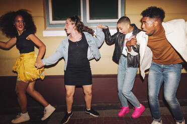 Playful friends having fun in the city at night. Group of vibrant young people dancing and having a good time together. Multicultural friends going out together on the weekend. - JLPSF09535