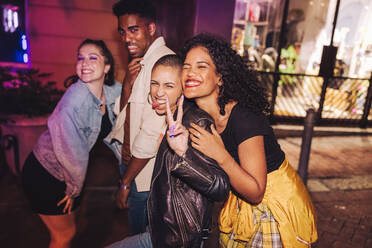 Eine Gruppe lebensfroher Freunde, die sich im Freien amüsieren. Multikulturelle junge Leute, die fröhlich in die Kamera lächeln, während sie nachts zusammenstehen. Fröhliche Freunde aus der Stadt, die am Wochenende abhängen. - JLPSF09548