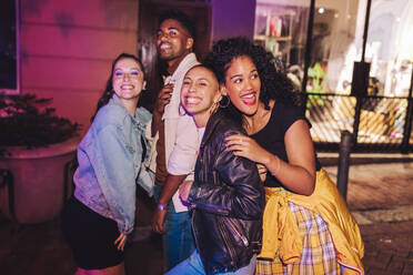 City friends having a good time outdoors. Group of multicultural young people smiling happily while standing together at night. Cheerful friends hanging out together on the weekend. - JLPSF09549