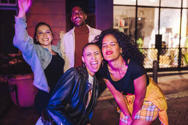 Energetic friends having fun together at night. Group of multicultural young people standing in neon light outdoors. Cheerful city friends hanging out together on the weekend. - JLPSF09551