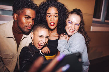 Capturing crazy weekend moments. Group of multicultural friends taking a group selfie while standing outdoors at night. Vibrant young people having a good time on the weekend. - JLPSF09563