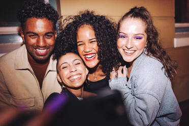 Taking happy selfies on friends night out. Group of multicultural friends taking a group selfie while standing outdoors at night. Cheerful young people having a good time on the weekend. - JLPSF09565