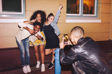 Freunde der Generation Z posieren für ein Foto vor einem Fotohandy. Eine Gruppe multikultureller Freunde hat Spaß, während sie nachts zusammen abhängen. Junge Leute machen glückliche Erinnerungen am Wochenende. - JLPSF09569