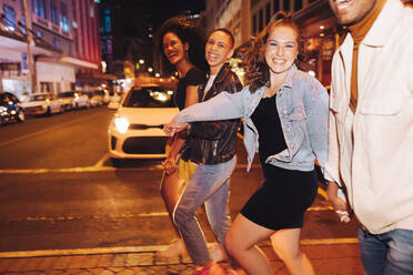 Generation Z friends going out together at night. Happy friends smiling cheerfully while crossing a road in the city. Group of vibrant young people having a good time on the weekend. - JLPSF09575