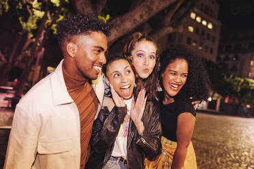 Happy young friends having a good time in the city at night. Group of multicultural young people hanging out together outdoors. Vibrant young people enjoying their weekend. - JLPSF09577