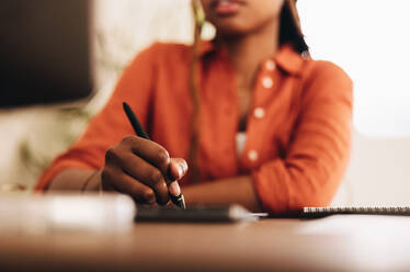 Eine Grafikdesignerin, die mit einem Stift zeichnet. Eine unerkennbare junge Frau, die an ihrem Schreibtisch vor einem Computer sitzt. Eine kreative Freiberuflerin, die in ihrem Büro zu Hause an einem neuen Projekt arbeitet. - JLPSF09628