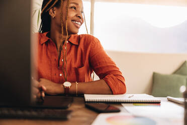 Lächelnde Designerin vor ihrem Computer sitzend. Glückliche junge Grafikdesignerin, die mit einem Stylus-Stift auf einem digitalen Tablet zeichnet. Kreative junge Frau, die in ihrem Heimbüro arbeitet. - JLPSF09632