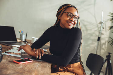 Imaginative young woman smiling in her home office. Happy young photographer thinking of new creative ideas for her project. Artistic female freelancer working at her desk. - JLPSF09676