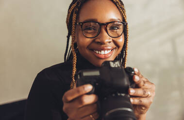 Ich habe eine Leidenschaft für die Fotografie. Glückliche Fotografin, die fröhlich lächelt, während sie eine Spiegelreflexkamera in ihrem Büro zu Hause hält. Künstlerische junge Freiberuflerin, die an einem neuen kreativen Projekt arbeitet. - JLPSF09682