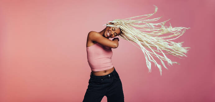 Portrait of happy woman dancing on pink background. Woman flying her long braided hair while dancing. - JLPSF09720