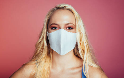 Close-up of a woman with protective face mask on pink background. Beautiful Female wearing protective face mask. - JLPSF09726