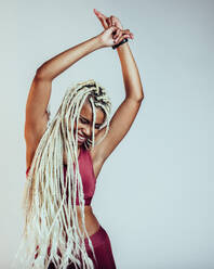 Porträt einer afrikanisch-amerikanischen Fitness-Frau, die mit den Händen in der Luft tanzt. Fröhliche Frau mit langen geflochtenen Haaren, die Spaß hat. - JLPSF09769