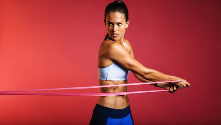 Slim athletic woman working on core strength training using resistance  band. Side view of fit woman doing workout using stretch band on maroon  background. stock photo