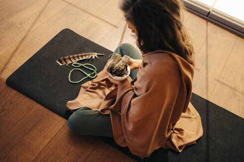 High angle view of a mature woman meditating with sage smudge sticks. Senior woman preparing to do an incense burning ceremony at home. Mature senior woman practicing alternative medicine. - JLPSF09815