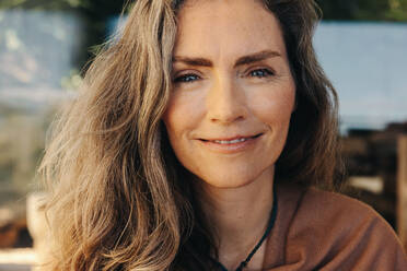 Portrait of a mature woman smiling at the camera while wearing a crystal necklace. Senior woman meditating and practicing self-healing at home. Happy mature woman living a holistic lifestyle. - JLPSF09818