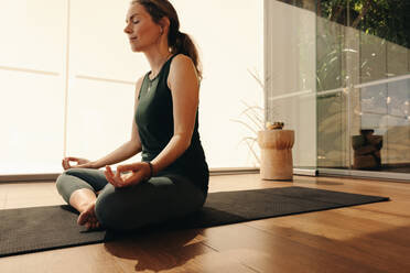 Ältere Frau meditiert, während sie Hatha-Yoga praktiziert. Ältere Frau, die eine Entspannungsübung macht, während sie in leichter Haltung sitzt. Frau, die ein gesundes Trainingsprogramm zu Hause verfolgt. - JLPSF09844