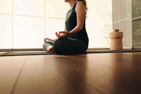 Ältere Frau beim Meditieren, während sie Hatha-Yoga praktiziert. Unerkennbare Frau, die eine Atemübung macht, während sie in entspannter Haltung sitzt. Ältere Frau, die ein gesundes Trainingsprogramm zu Hause absolviert. - JLPSF09845