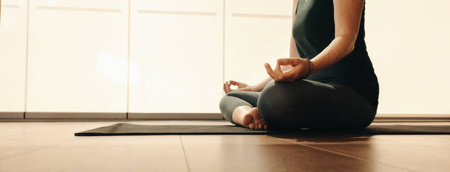 Ältere Frau meditiert während einer Hatha-Yoga-Sitzung. Unbekannte Frau, die eine Entspannungsübung macht, während sie in entspannter Haltung sitzt. Ältere Frau, die zu Hause ein gesundes Trainingsprogramm absolviert. - JLPSF09846
