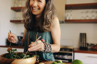 Lächelnde Seniorin, die sich in ihrer Küche eine köstliche Buddha-Schale gönnt. Aufgeregte Frau, die sich zu Hause gesundes veganes Essen serviert. Reife Frau, die ihren alternden Körper mit einer pflanzlichen Ernährung pflegt. - JLPSF09852