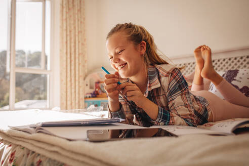 Lächelndes Mädchen auf dem Bett liegend mit Büchern. Mädchen studiert, während sie auf dem Bett zu Hause liegt. - JLPSF09885