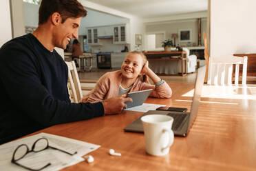 Glücklicher junger Mann, der mit seiner Tochter am Tisch sitzt und zu Hause ein digitales Tablet benutzt. - JLPSF09891