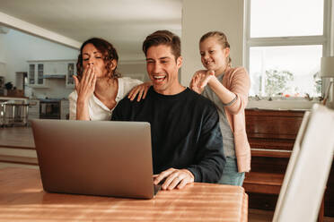 Eine dreiköpfige Familie führt zu Hause ein Videogespräch auf dem Laptop. Vater, Mutter und Tochter unterhalten sich gemeinsam online auf dem Laptop. - JLPSF09924