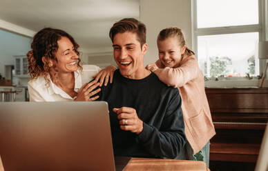 Familie führt zu Hause einen Videoanruf durch. Ein Paar mit seiner Tochter sitzt vor einem Laptop und führt einen Videoanruf durch. - JLPSF09925