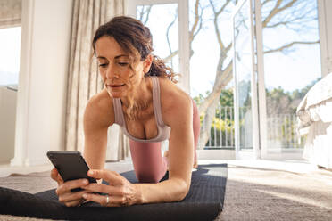 Eine Frau macht Yoga auf einer Matte und nutzt eine Online-Sitzung auf ihrem Handy. Eine Frau trainiert zu Hause in Corona Virus Pandemie. - JLPSF09930