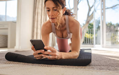 Frau schaut in das Telefon Online-Yoga-Kurse während der Ausübung. Weiblich in Sportkleidung mit ihrem Telefon zu finden Workout-Tutorials online. - JLPSF09931