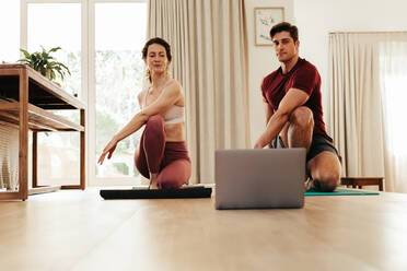 Paar Stretching beobachten Fitness-Video-Tutorial online auf Laptop. Fit Mann und Frau tun Yoga-Training zu Hause sitzen auf Matte im Wohnzimmer üben Yoga Seite Twist Übung. - JLPSF09942