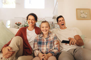 Family watching comedy movie on television at home. Father, mother and daughter sitting at home watching tv and laughing. - JLPSF09949