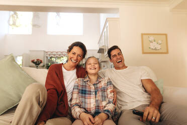 Lächelnde Familie sitzt auf dem Sofa und genießt das Fernsehen zu Hause. Eine dreiköpfige Familie entspannt sich zu Hause vor dem Fernseher. - JLPSF09951