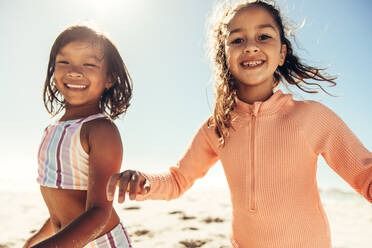 Energetic little girls smiling at the camera while playing around at the beach. Two adorable little girls having fun together during summer vacation. - JLPSF09960