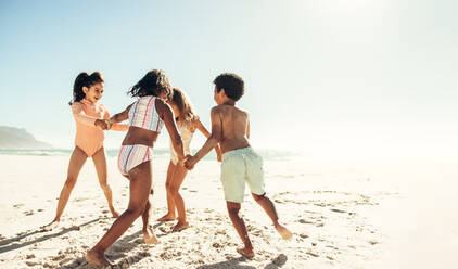 Glückliche junge Freunde, die fröhlich lachen, während sie ein Spiel am Strand spielen. Gruppe von energiegeladenen kleinen Kindern, die in den Sommerferien zusammen Spaß haben. - JLPSF09969