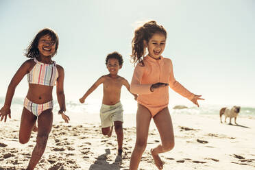 Glückliche junge Freunde, die fröhlich lachen, während sie am Strand spielen. Eine Gruppe liebenswerter kleiner Kinder, die Spaß haben und ihre Sommerferien genießen. - JLPSF09974