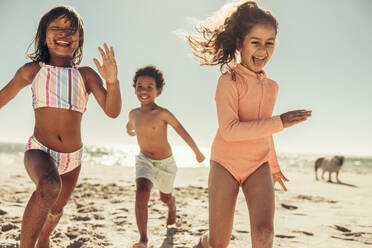 Glückliche junge Freunde, die fröhlich lachen, während sie am Strand spielen. Eine Gruppe liebenswerter kleiner Kinder, die Spaß haben und ihre Sommerferien genießen. - JLPSF09975