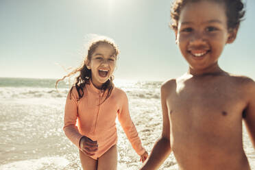 Zwei entzückende kleine Kinder lachen fröhlich, während sie am Strand spielen. Zwei fröhliche junge Kinder, die sich in den Sommerferien vergnügen. - JLPSF09978